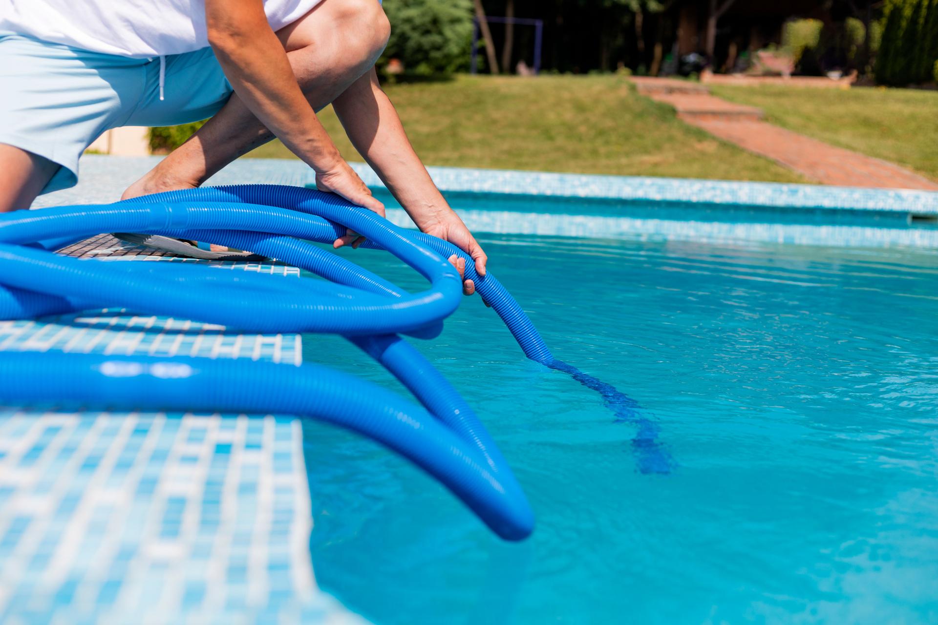 Pool technician checking data on a tablet beside a swimming pool with chemical containers and lush greenery.